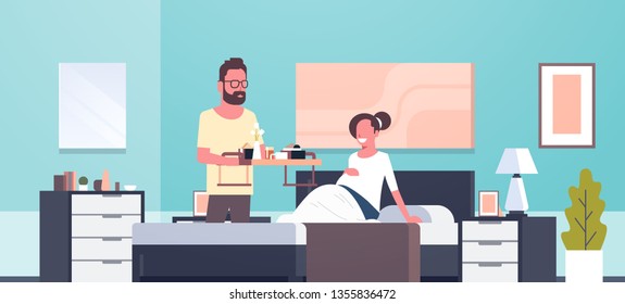 Husband Bringing Breakfast Tray For Pregnant Wife Sitting On Bed Man Serving Food Happy Family Modern Home Bedroom Interior Future Parents In Love Full Length Horizontal