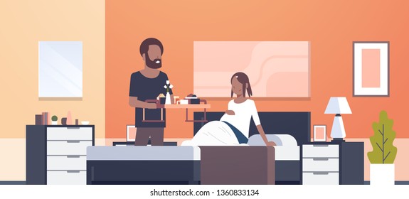 husband bringing breakfast tray for pregnant wife sitting on bed man serving food happy african american family modern home bedroom interior future parents in love full length horizontal