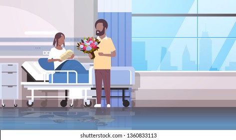 husband holding flowers bouquet for his wife with newborn baby loving father visiting new born child happy african american family parenthood concept hospital ward interior horizontal