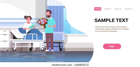 husband holding flowers bouquet for his wife with newborn baby sitting on bed father visiting new born child happy family parenthood concept hospital ward interior horizontal copy space