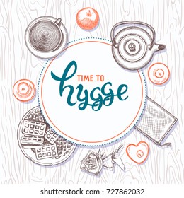 Hygge is a Danish living style. Vector background with hand drawn illustrations cozy home things: candles, teapot, cup with tea and waffle, apples on wooden texture. Lettering time to hygge.