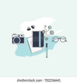 Illustrated feminine workplace in top view perspective with blue and white paint splatter, camera, notebooks, eucalyptus plant, eyeglasses and paper clips.