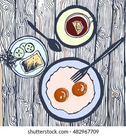 Illustration with breakfast. Fried eggs, tea with lemon, cucumber, potherbs, bread, plates, dishes, spoon, fork. Wooden surface.Seen from above.