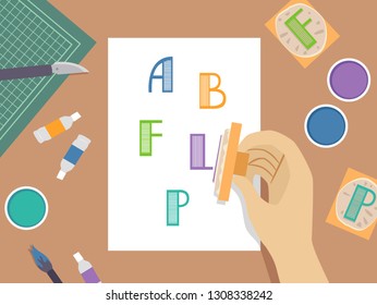 Illustration of a Hand Holding a Letter Stamp Pad Over Paper with Colored Inks On Table