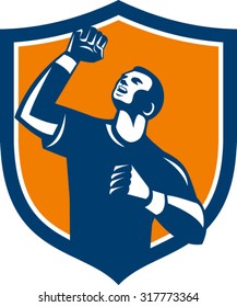 Illustration of a male athlete doing a fist pump looking up viewed from low angle set inside shield crest on isolated background done in retro style. 