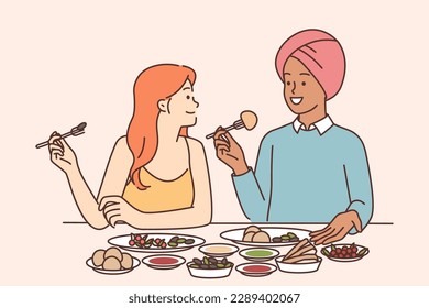 Indian man and caucasian woman are sitting at dinner table tasting traditional Indian cuisine with spices. Multicultural couple having dinner together in restaurant tasting national dishes