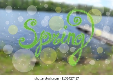 inscription Spring is a black gel pen. Inscription with curls on blurred background of a summer landscape with a small river, trees