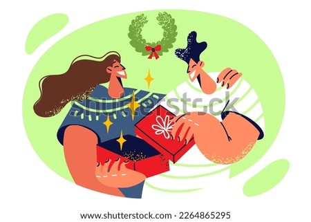 Intrigued man opens box with Christmas present from girl or mother standing behind and hugging son. Teenage guy looking forward to making unboxing gift on Christmas Eve or New Year holidays 