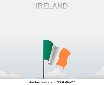 The Irish flag flutters on a pole standing tall against a white sky