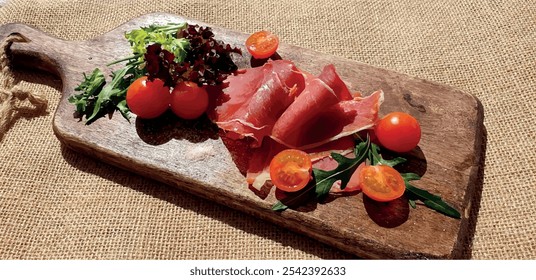 Jamon sliced ​​on a wooden board with tomatoes and herbs. Spanish jamon on the board. Appetizing jamon plate. Ham slice. Pork meat. Dried meat with vegetables.