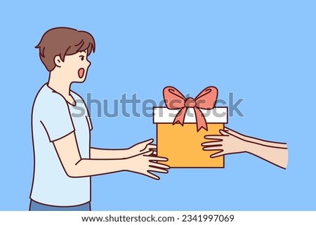 Joyful boy receives gift box with red ribbon on eve of birthday or christmas holidays. Hands with big gift box near teenager schoolboy, for concept of present or award for academic achievement