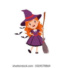 Joyful red-haired girl witch standing with broom and wearing purple dress and hat. Kid character in costume surrounded with black bats. Vector flat cartoon illustration on white.