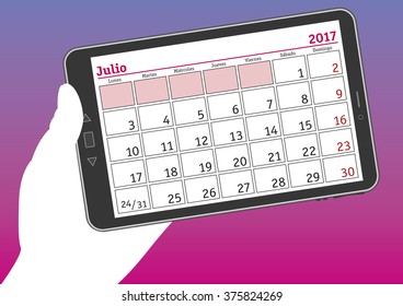 July 2017, julio 2017. A hand holds a tablet pc with a calendar sheet in spanish. 