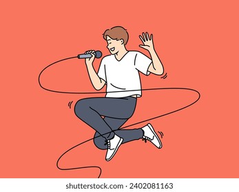 Jumping male singer with microphone enjoys performing energetic songs at karaoke party. Popular singer performing at concert and smiling while singing solo pop or hip hop composition.