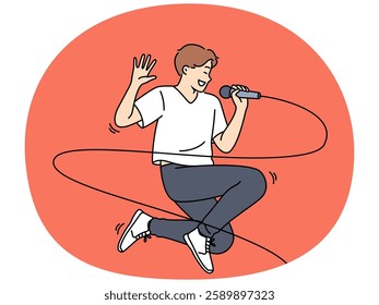 Jumping male singer with microphone enjoys performing energetic songs at karaoke party. Popular singer performing at concert and smiling while singing solo pop or hip hop composition.