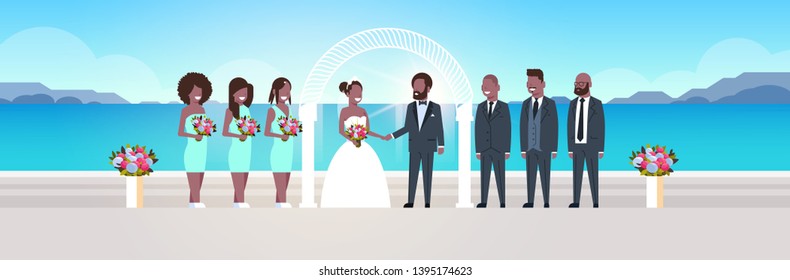 just married african american bride and groom with bridesmaids groomsmen standing together sea beach arch wedding ceremony concept sunrise mountains background full length horizontal