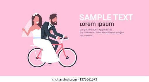 just married man woman riding bicycle romantic couple bride and groom cycling bike having fun wedding day concept pink background copy space full length horizontal flat