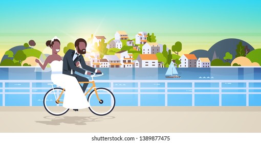 just married man woman riding bicycle romantic african american couple bride groom cycling bike having fun wedding day concept mountain city island background full length horizontal flat