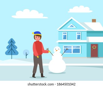 Kid walking in winter clothes outside. Happy boy in warm clothes standing against the background of a snowy house. Outdoor leisure activity. Male character on the street is sculpting a snowman