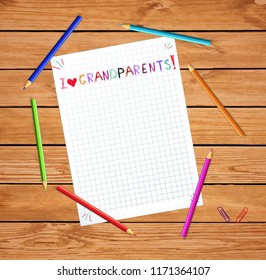 Kids colorful hand drawn lettering I love grandparents on notebook sheet or graphing paper on wooden tabel with colored pencils around. Greeting card template, frame, border with copy space.