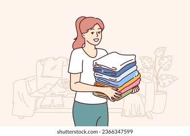 Kind woman housewife collects unwanted clothes around apartment to donate wardrobe items to charitable foundation. Housewife stands in room with scattered clothes and neatly stacks t-shirts in pile