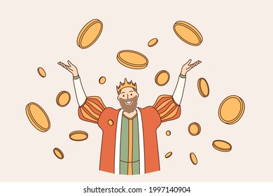 King of coins wealth concept. Young smiling man king in crown cartoon character standing with hands raised up in flying around golden coins feeling happy and confident 