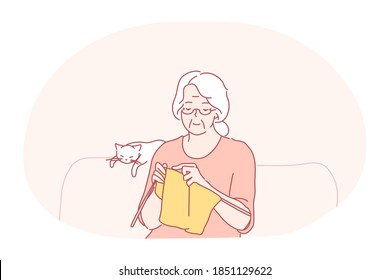 Knitting, hobbies of elderly people concept. Smiling grey haired senior woman grandmother sitting and knitting scarf from wool on sofa with sleeping cat nearby. Pastime, leisure, grandparents
