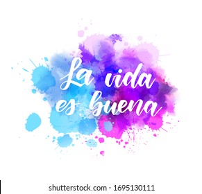 La vida es buena (Life is good in Spanish) - handwritten modern calligraphy lettering on abstract watercolor painted splash background. Blue and purple colored.