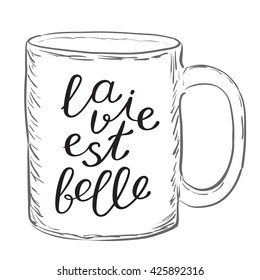 La vie est belle. Life is good in French. Brush hand lettering. Handwritten words on a sample mug. Great for mugs, posters, throw pillow cases, t-shirts design, home decor and more.