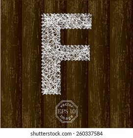 Letter F, made with threads on pins on wooden background