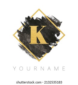 Letter K logo design. Black watercolor brush stroke with gold letter and gold square frame.
