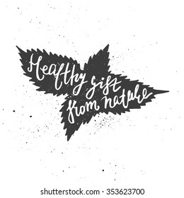 Lettering composition. Phrase Healthy gift from nature inscribed into nettle leaves silhouette. Ink splashes on white background.
