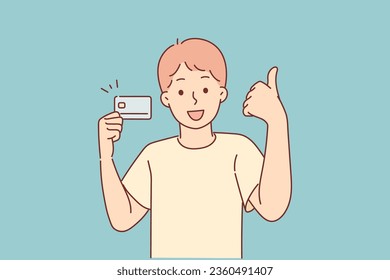 Little boy with credit card shows thumbs up recommending to start using banking services from early age. Child demonstrates child credit card for buying school lunches or going to cinema with friends