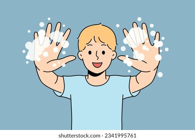 Little boy with foam shows soapy palms, recommending washing hands and following hygiene rules. Happy teenage boy doing preventive diseases and using soap after returning from school or walking