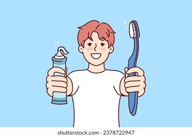 Little boy holds toothpaste and toothbrush showing snow-white smile and recommending brushing teeth regularly. Child independently monitors health of own teeth in order to get rid of caries