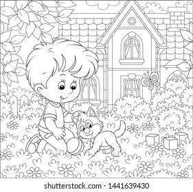 Little boy playing with a cute small kitten among flowers on a lawn in front of his house on a sunny summer day, black and white vector illustration in a cartoon style