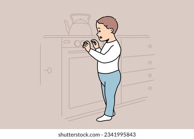 Little boy plays with gas stove and touches dangerous kitchen equipment while parents are away. Curious child toddler studies stove with interest and needs supervision to avoid accident