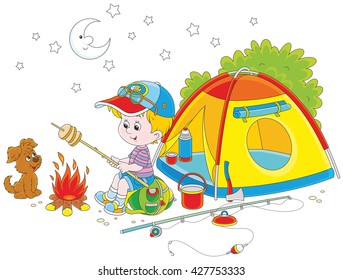 Little boy scout roasting bread on campfire near his camping tent