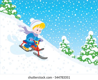 Little boy sliding down the snow hill on his small snow-scooter