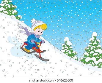 Little boy sliding down the snow hill on his small snow-scooter