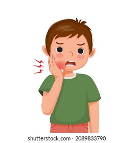 Little Boy Suffering From Toothache Touching His Cheek Feeling Painful. Kid With Dental Problem And Sensitive Teeth Showing Upset Facial Expression