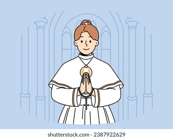 Little catholic girl takes part in first holy communion and stands in temple making prayer gesture. Child dressed for christian religious ritual of holy communion inside cathedral. 