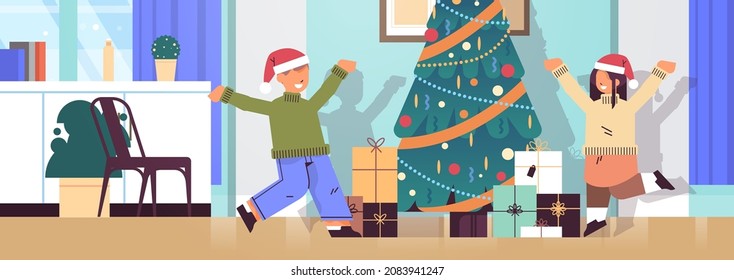 little children in santa hats happy to found gifts near fir tree new year christmas holidays celebration concept