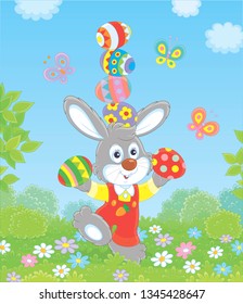 Little Easter bunny juggling with colored eggs among flowers on green grass of a lawn on a sunny spring day, vector illustration in a cartoon style