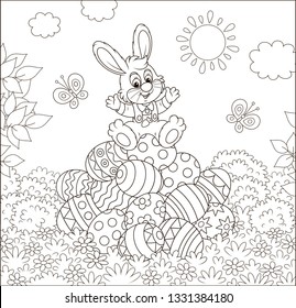 Little Easter Bunny on a pile of colorfully decorated eggs on grass on a sunny spring day, black and white vector illustration in a cartoon style for a coloring book
