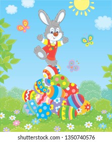 Little Easter Bunny on a pile of colorfully decorated eggs on green grass on a sunny spring day, vector illustration in a cartoon style