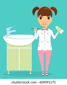 Little girl brushing her teeth standing near the washbasin. Girl dressed in pajamas. Hygiene and health. Happy child