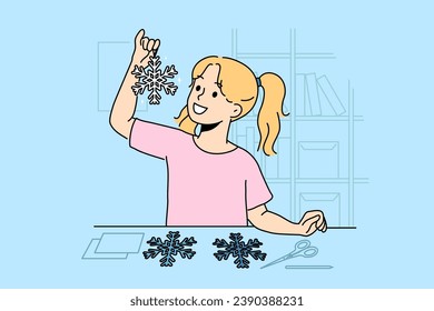 Little girl cuts out paper snowflakes preparing handmade christmas decorations for home on eve of new year. Child stands near table with scissors demonstrating snowflake made with own hands