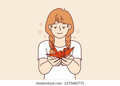 Little girl holds origami swan in hands, made together with school teacher at lesson in creative skills. Happy teenage child is addicted to origami, and shows fake symbolizing peace and prosperity