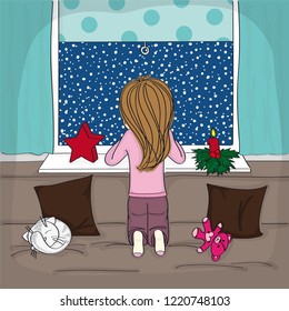 Little girl kneeling on the sofa in the cosy and warm living room, looking out of the window to the night winter scenery, her cat is sleeping safe and sound on the sofa. The snow is falling ouside.